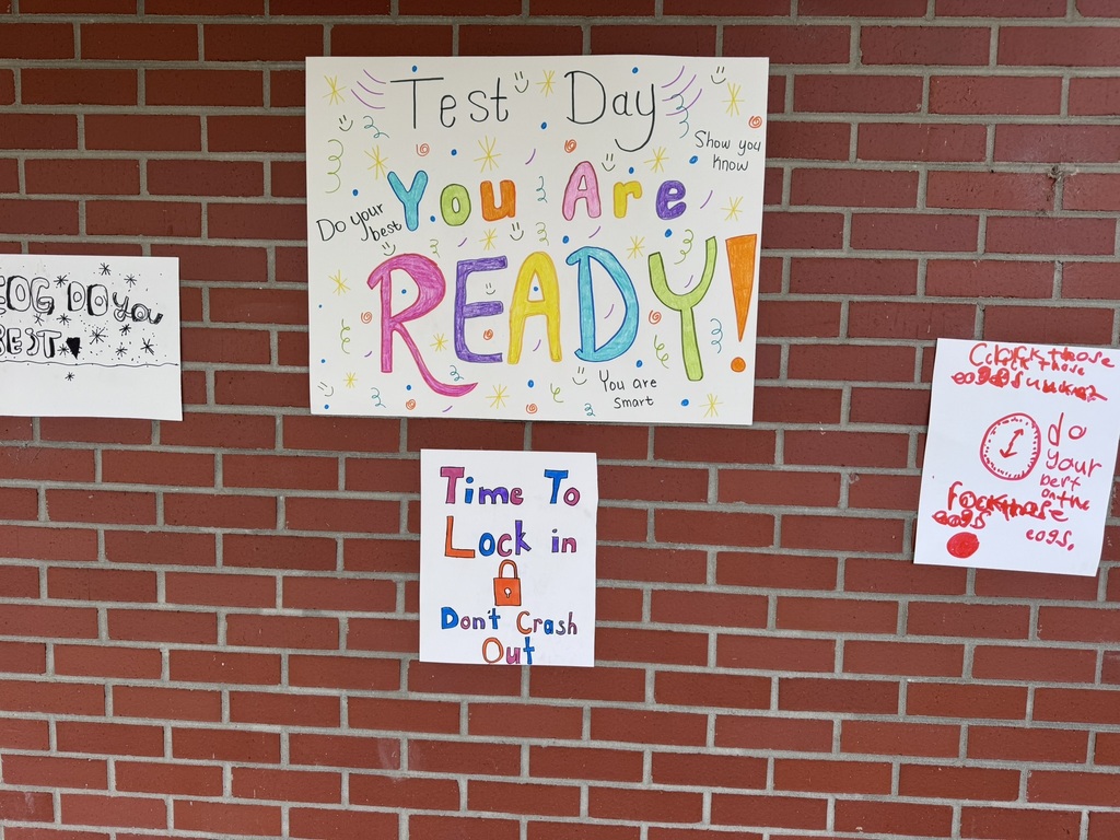 A bright and cheerful student-made poster hangs on a brick wall reading “Test Day You Are READY!” in rainbow-colored letters surrounded by stars, swirls, and encouraging notes for students taking the EOG test.
