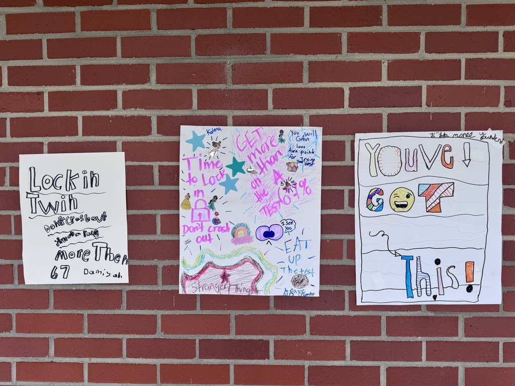 A bright and cheerful student-made poster hangs on a brick wall reading “Test Day You Are READY!” in rainbow-colored letters surrounded by stars, swirls, and encouraging notes for students taking the EOG test.