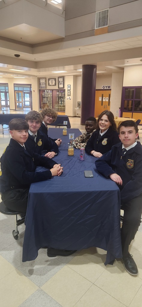 A close-up of  West Bladen FFA students wearing official blue and gold jackets, smiling and sitting together at a banquet table.