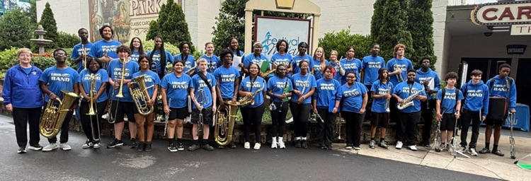 A group of students in matching blue shirts that say EBHS Band. Many students are holding musical instruments.