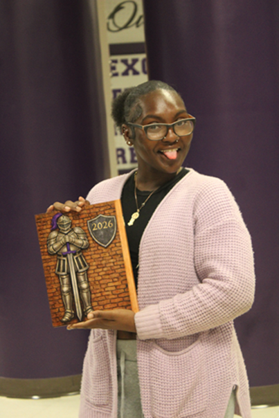 Student poses with a section of the 2026 yearbook cover featuring a knight illustration and shield. The artwork was inspired by the student's original design contribution to this year's yearbook.