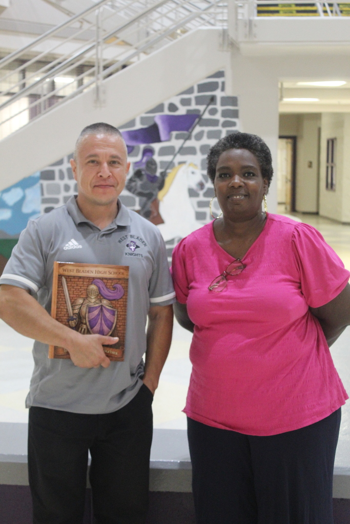 Mr. Salvador Garcia, recipient of the 2026 yearbook dedication, stands with teacher Lara Barber while holding a copy of the 2026 yearbook in the lobby of West Bladen High School.