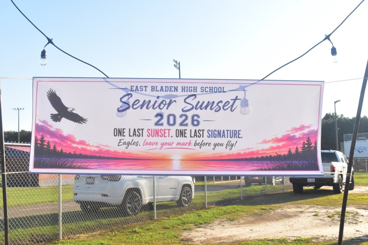 White banner hanging that displays the sunset setting at the bottom and equal flying and Reads senior sunset 2026