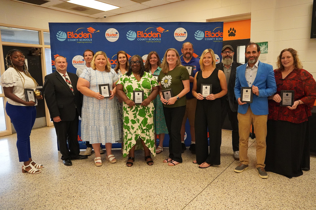 A group of educators stand together smiling while holding plaques. 