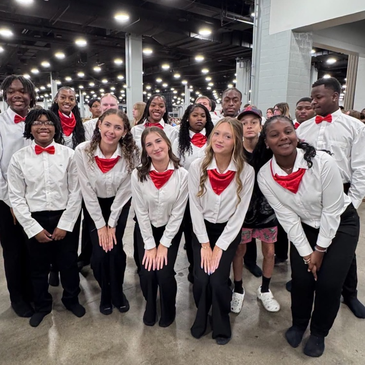 diverse group of young people standing together indoors, wearing matching white button-down shirts, black pants, and bright red bow ties or neckerchiefs.