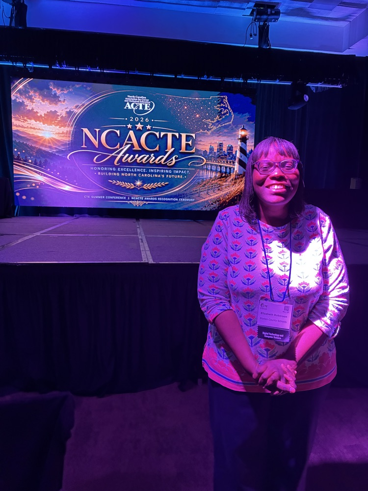 An educator stands in front of a stage, with a presentation slide behind her that reads “NCACTE Awards"