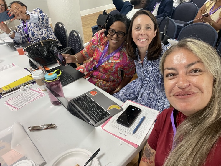 Three adult women sit together smiling at a table.