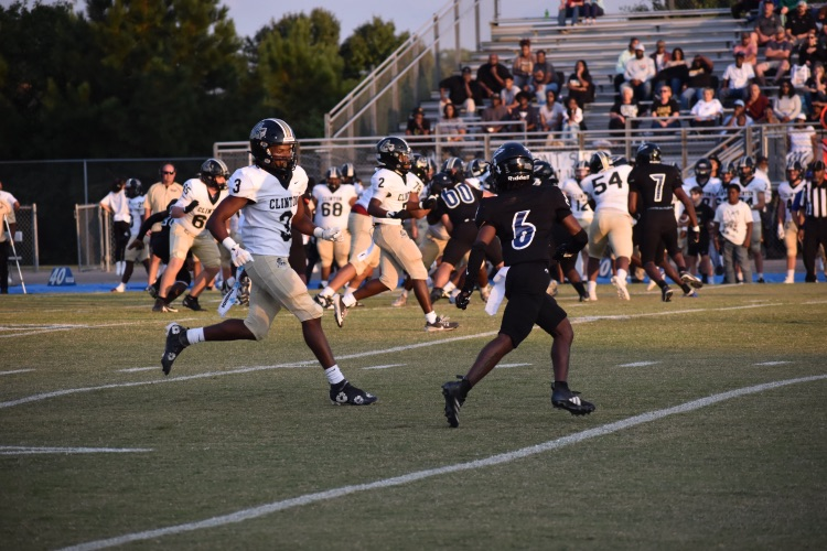 Photo of football players in a game on a green turf field with white stripes, there are players in black jerseys and players and white jerseys