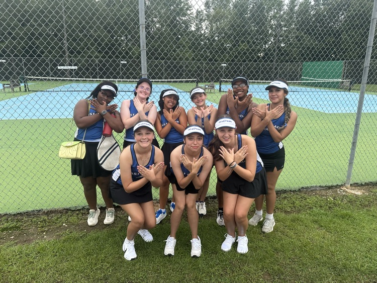 tennis players in black skirts and blue shirts with tennis rackets making an eagle with their hands 