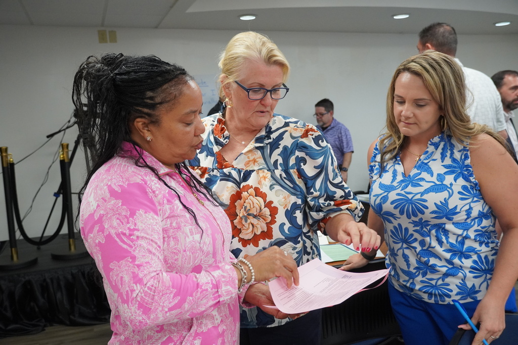 Three female professionals stand together reviewing a document.
