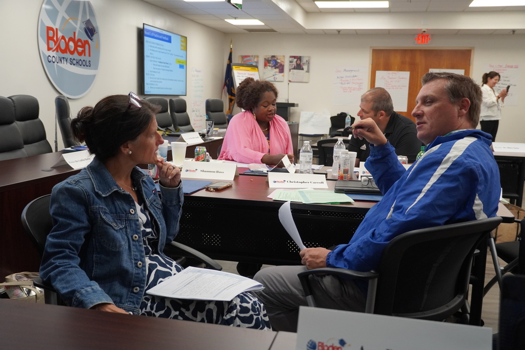 Four school administrators are sitting in chairs around a table. They are working in pairs.