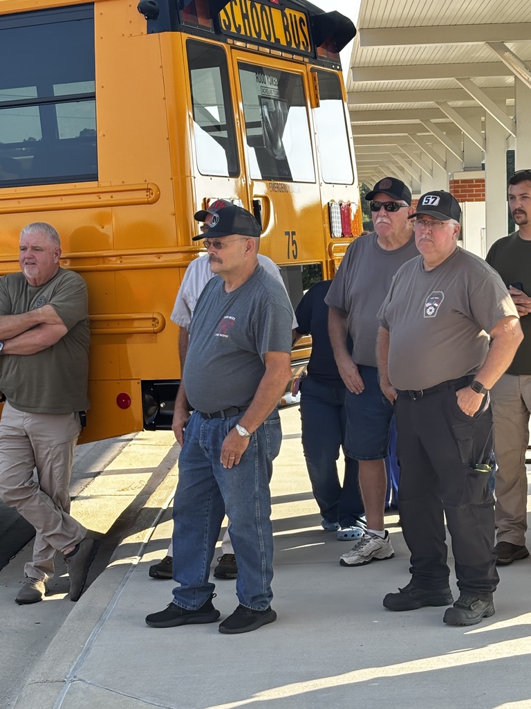 A small group of adults stand together behind a school bus.