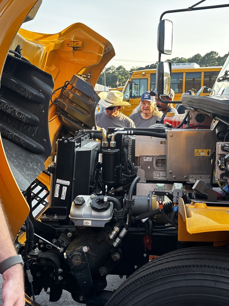 The front of an electric bus is open, so that a group of onlookers can view what is inside during a training session.