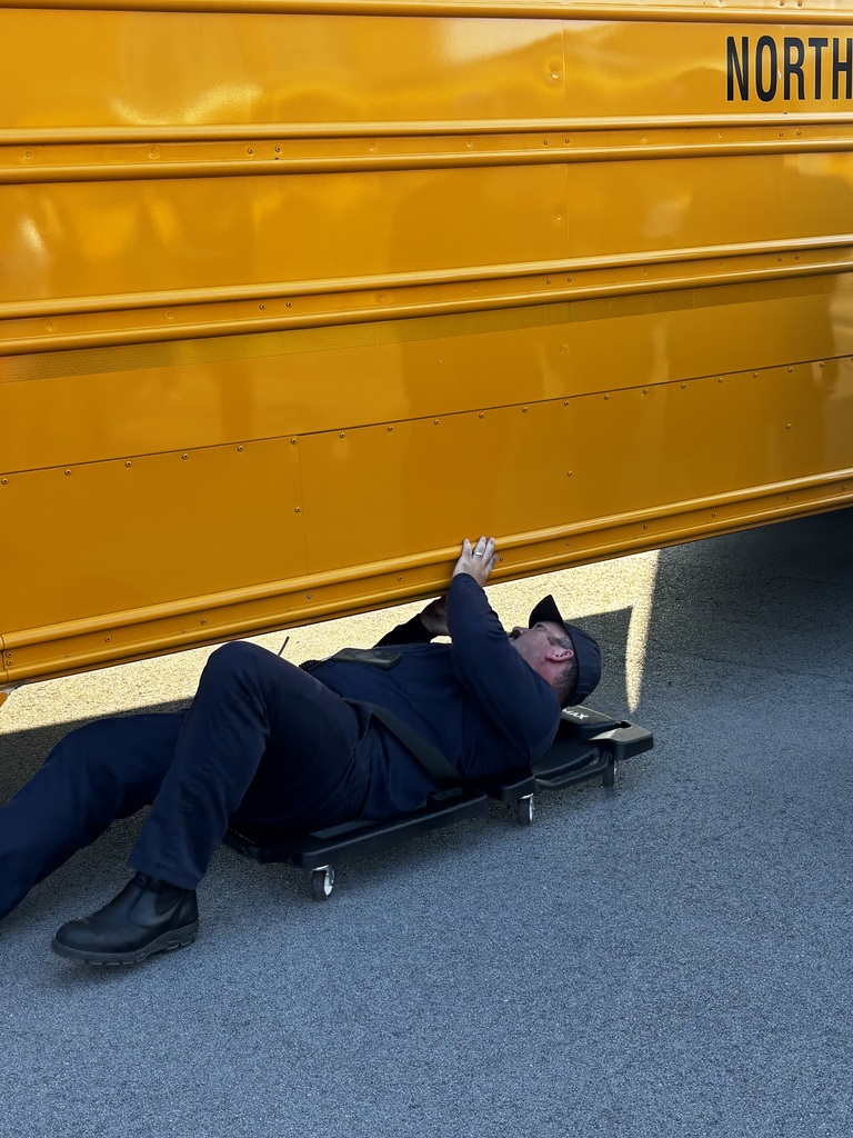An adult is on a wheeled board looking under a school bus.