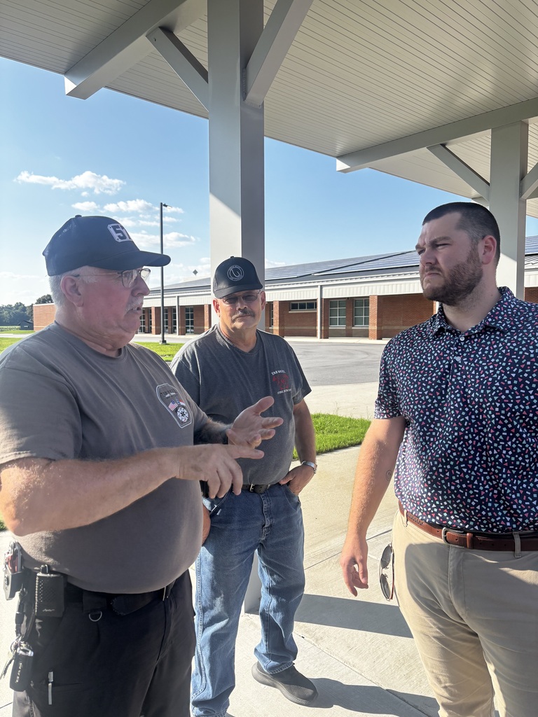 3 adults talking together under a walkway in front of a school.