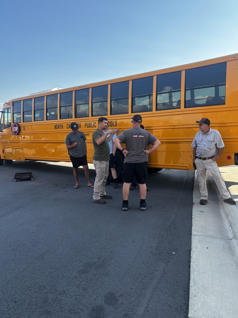 5 adults standing beside an electric school bus talking together.