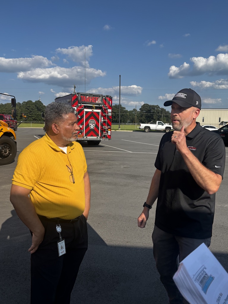 Two adults talking in a parking lot. Behind them is a Tar Heel EMS vehicle.