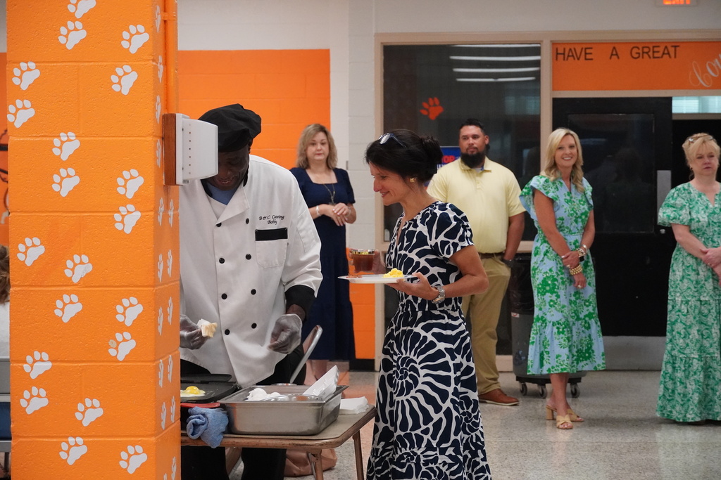 Adults are standing in line for the breakfast buffet, while one adult is standing next to a chef preparing eggs.