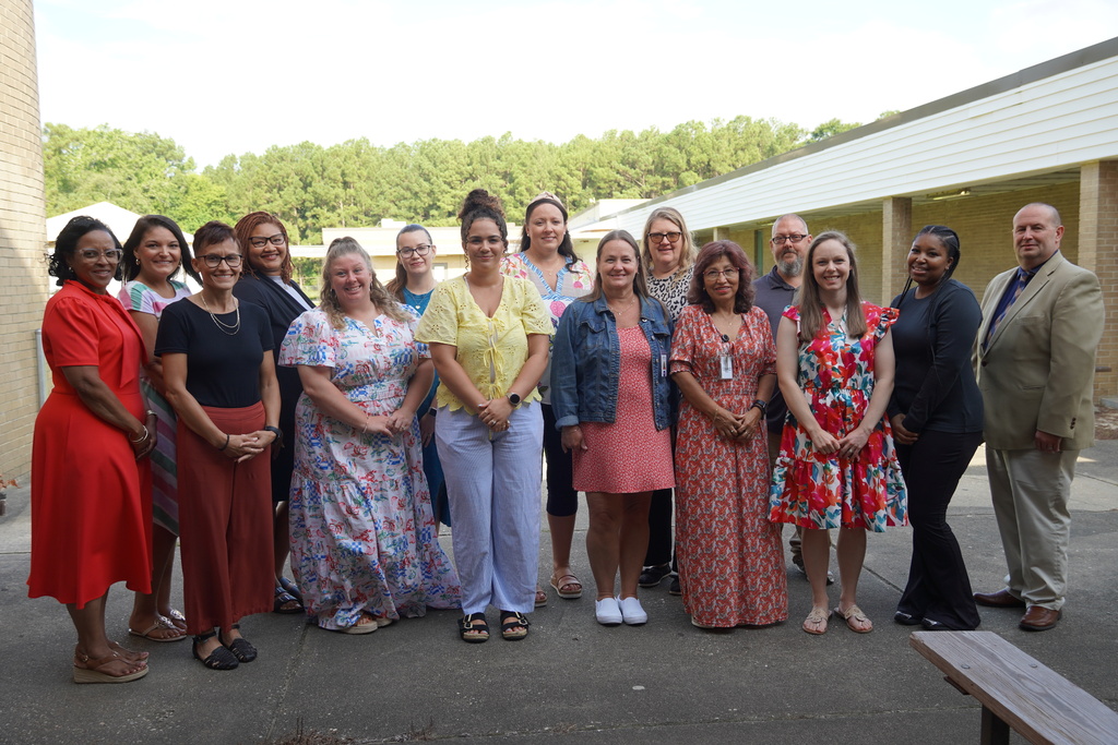 A group of adults stand together smiling outside. 
