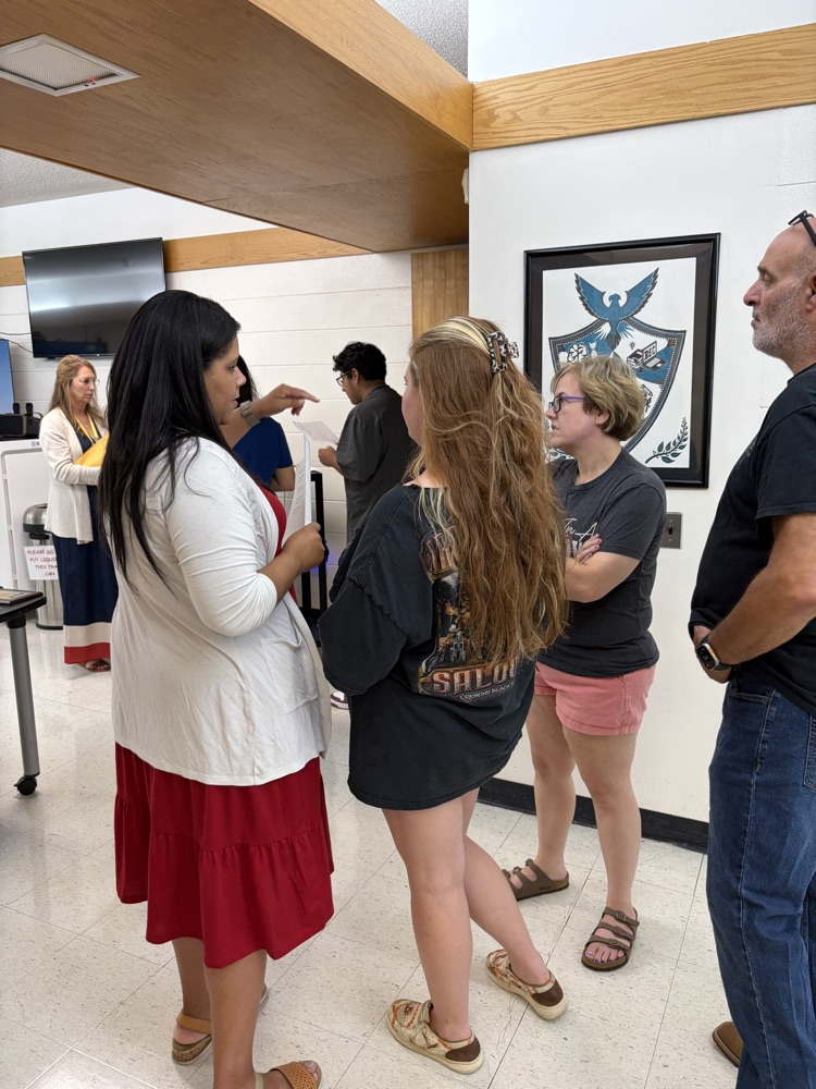 A teacher speaks with a student and family in the hallway.