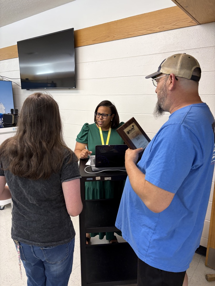 A student and parent stand speaking with a staff member at a computer .