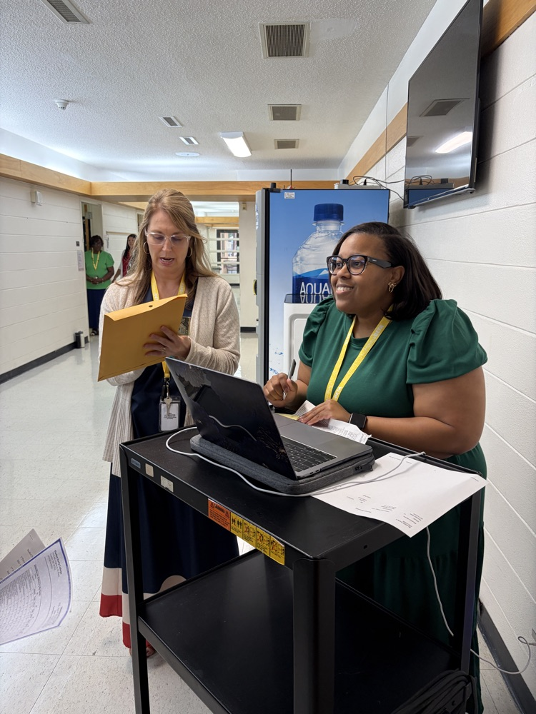 Two staff members stand together in a school hallway.