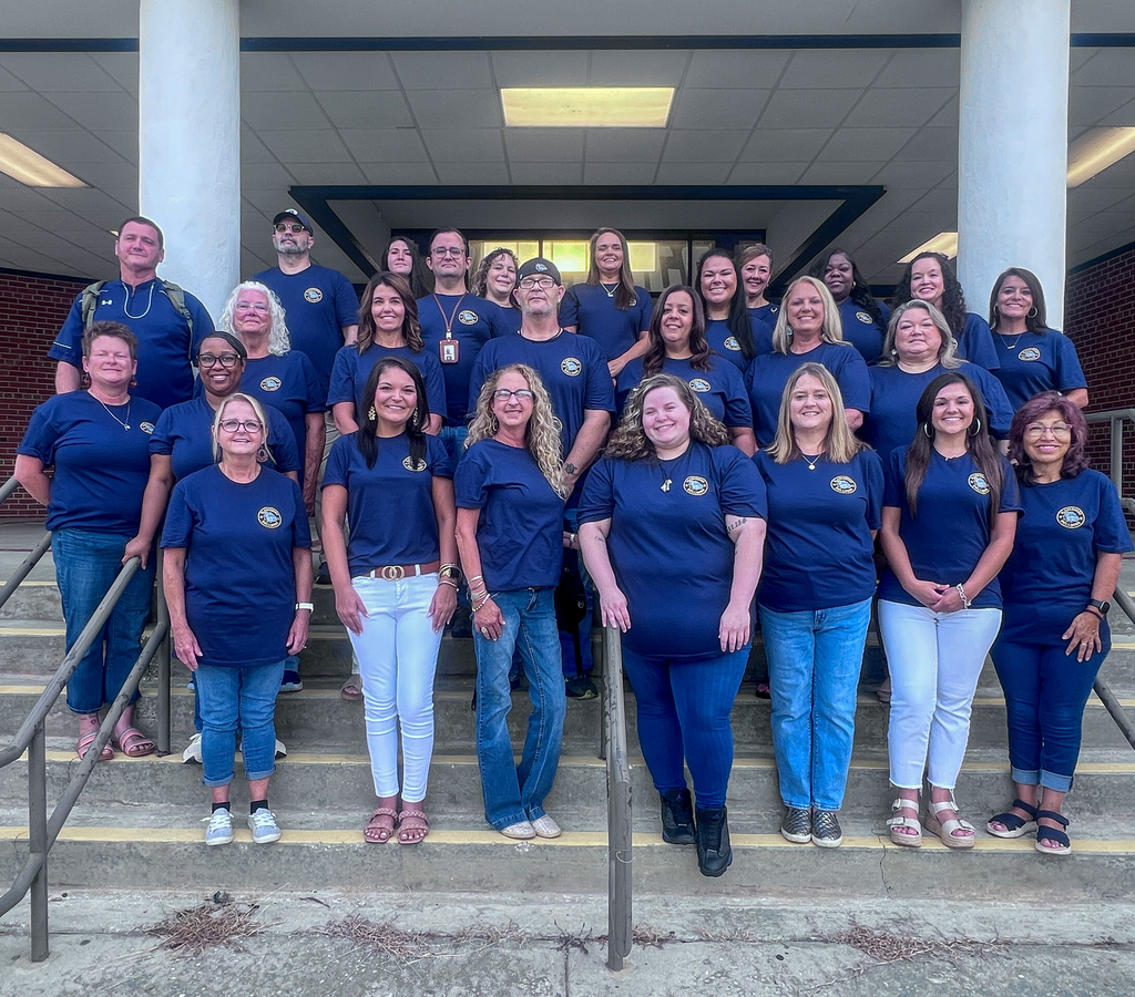Group photo of Bladenboro Middle School staff members wearing matching navy blue shirts, gathered on the front steps of the school. Staff members smile for the camera, showing Bulldog pride and unity as they prepare for the new school year.