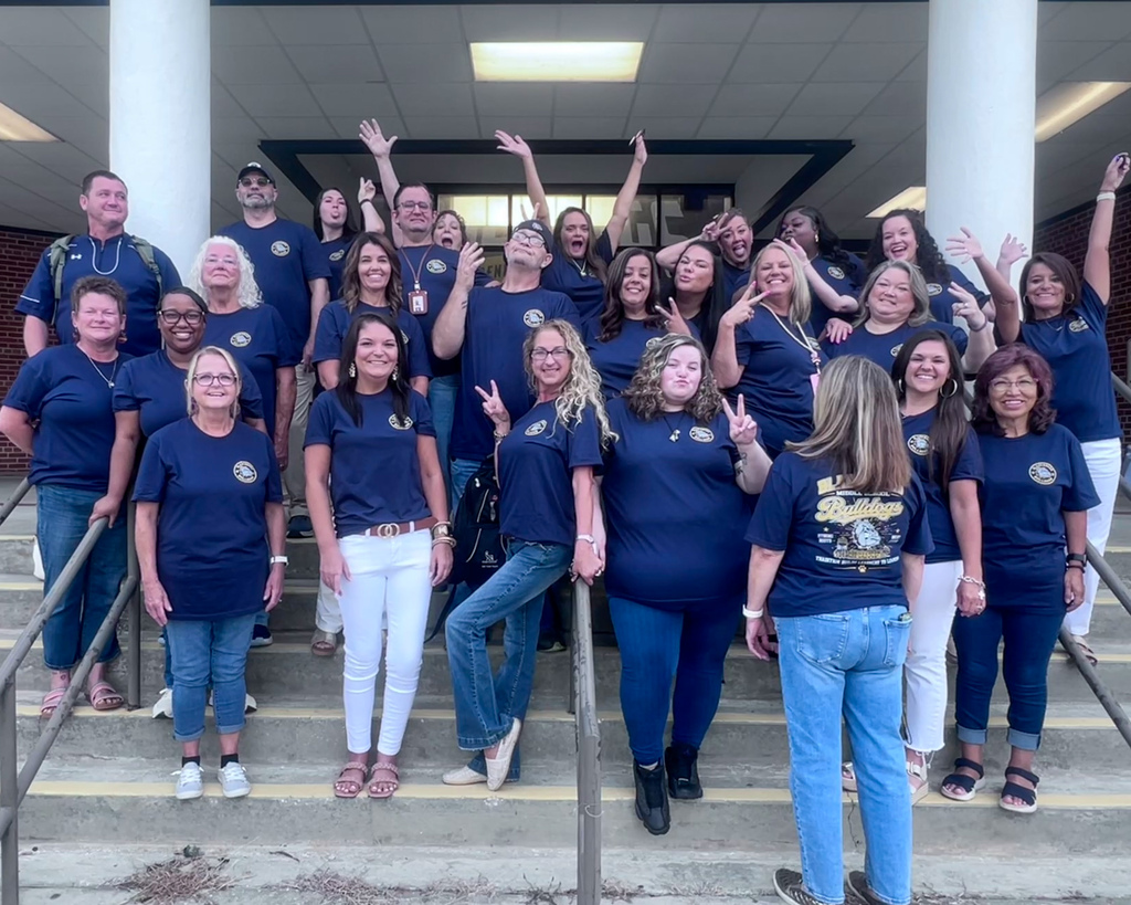 Bladenboro Middle School staff members show their fun side while posing on the school steps in matching navy shirts. Smiles, peace signs, raised hands, and playful poses capture the energy, personality, and Bulldog spirit of the BMS team.