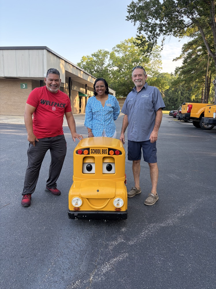 Three staff members stand with Buster, the transportation departments mini bus.