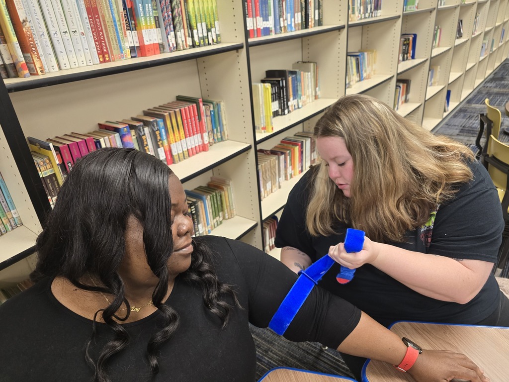 Two BMS staff members practice applying a tourniquet during hands-on Stop the Bleed training in the school media center.