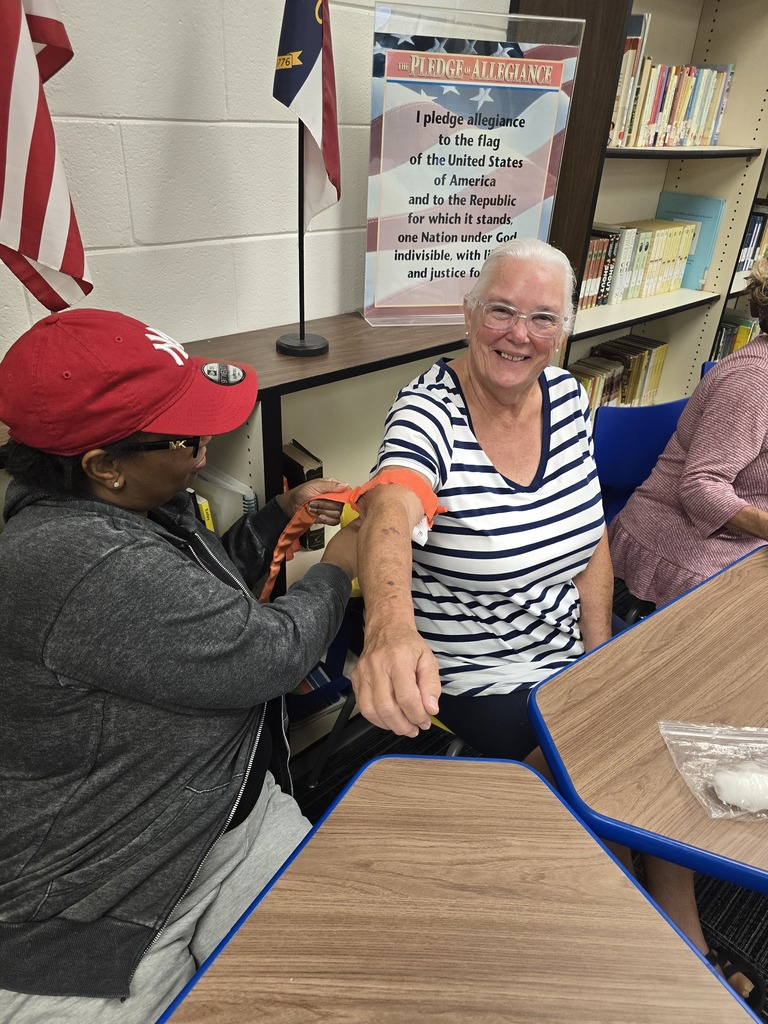Two BMS staff members practice applying a tourniquet during hands-on Stop the Bleed training in the school media center.