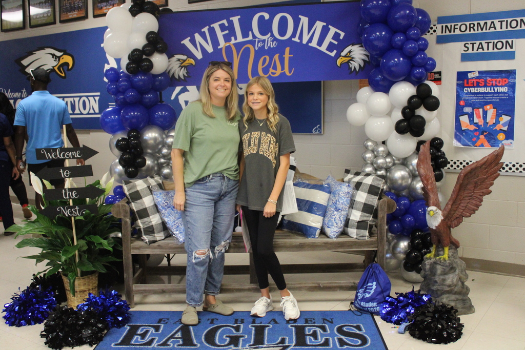An East Bladen High School student and parent stand smiling in front of a Welcome to the Nest sign with a school themed balloon arch.