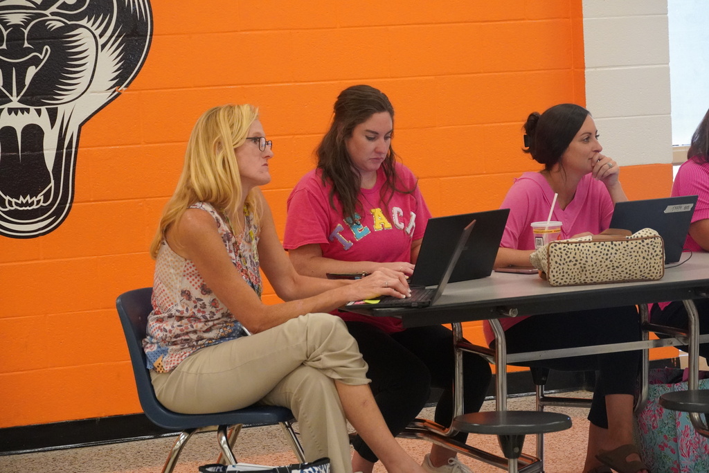 Three employees are seen working on laptops in a school cafeteria.