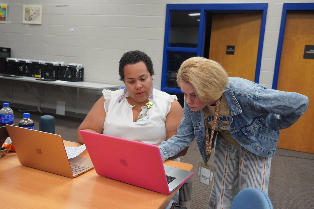 Two staff members are collaborating at a table with two laptops.