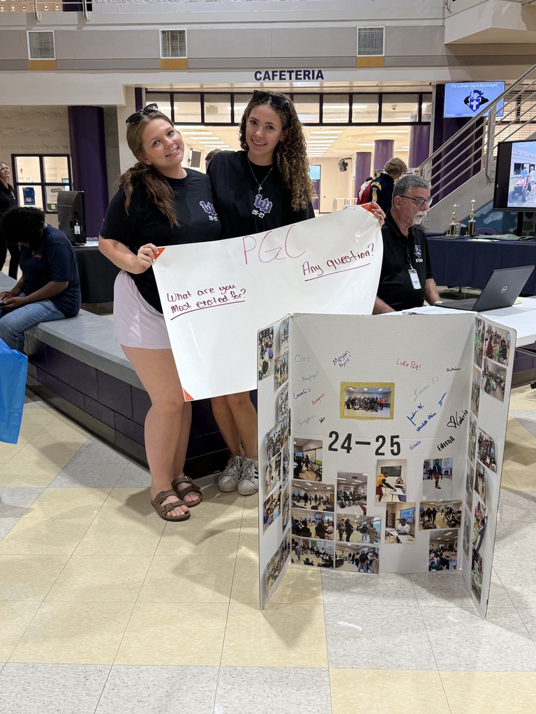 Two smiling students hold a PGC sign asking "What are you most excited for?" and "Any question?" inside the school atrium
