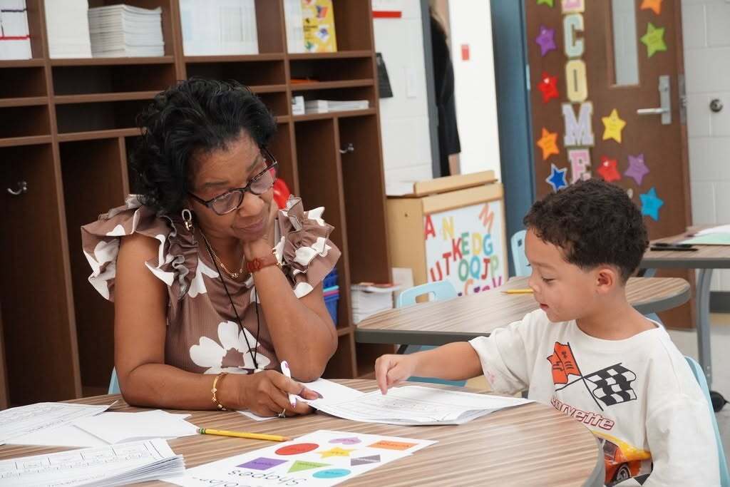 A teacher and young student are reviewing work together at a table.