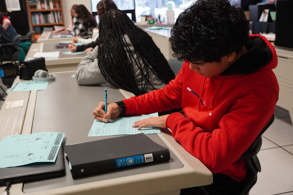 A high school student is working with paper and pencil at a table.