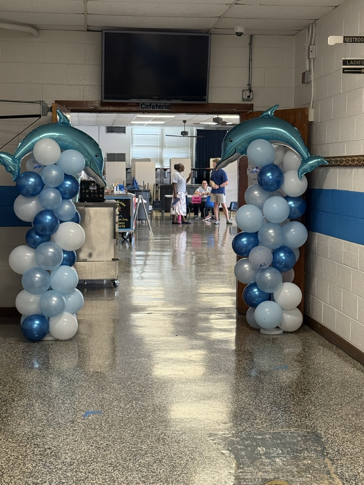     Blue and white balloon columns topped with dolphin balloons welcome families into the school cafeteria for Open House.