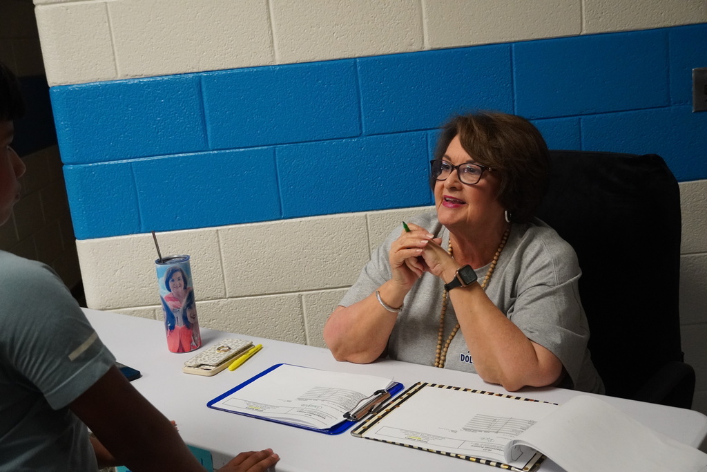 A staff member sits smiling at a desk to greet families.