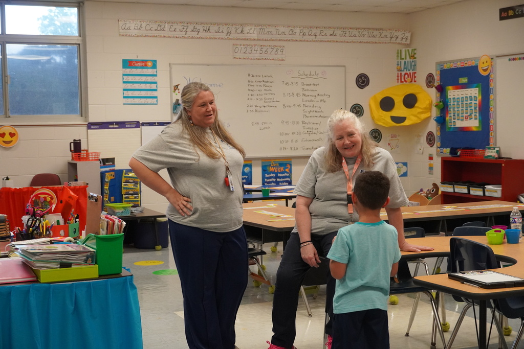 Two smiling teachers speak to a student in a well decorated classroom.