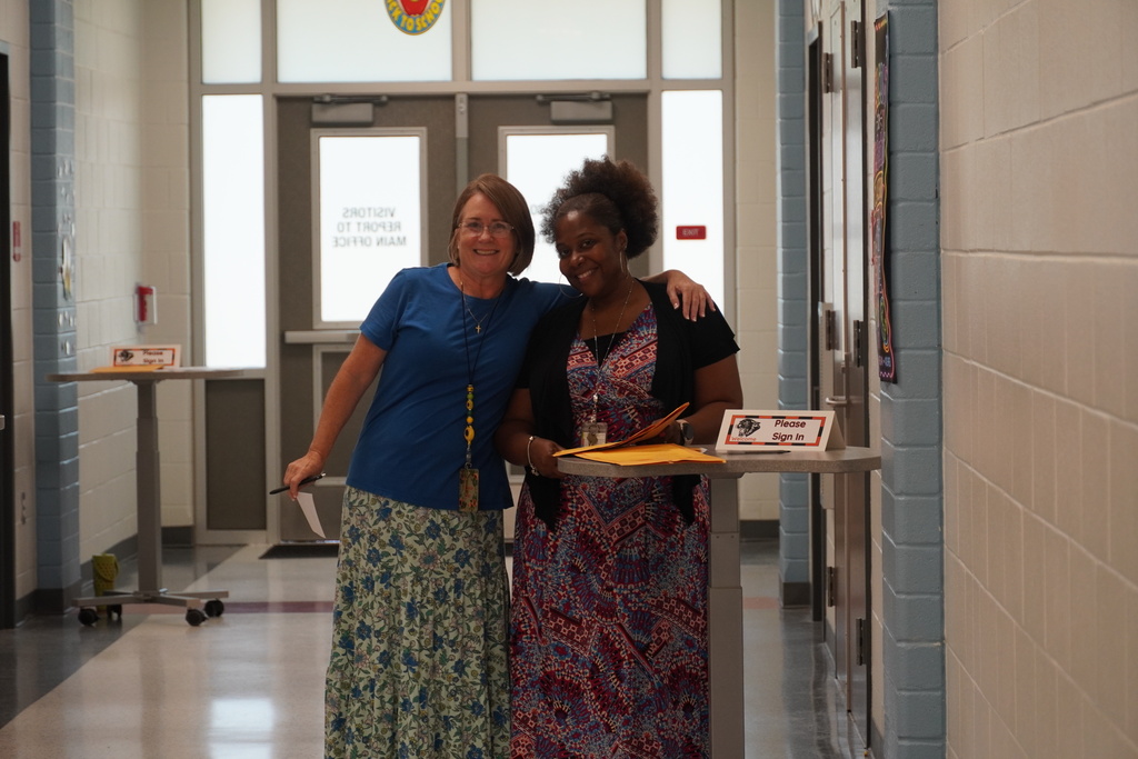Two teachers stand together smiling in the hallway.