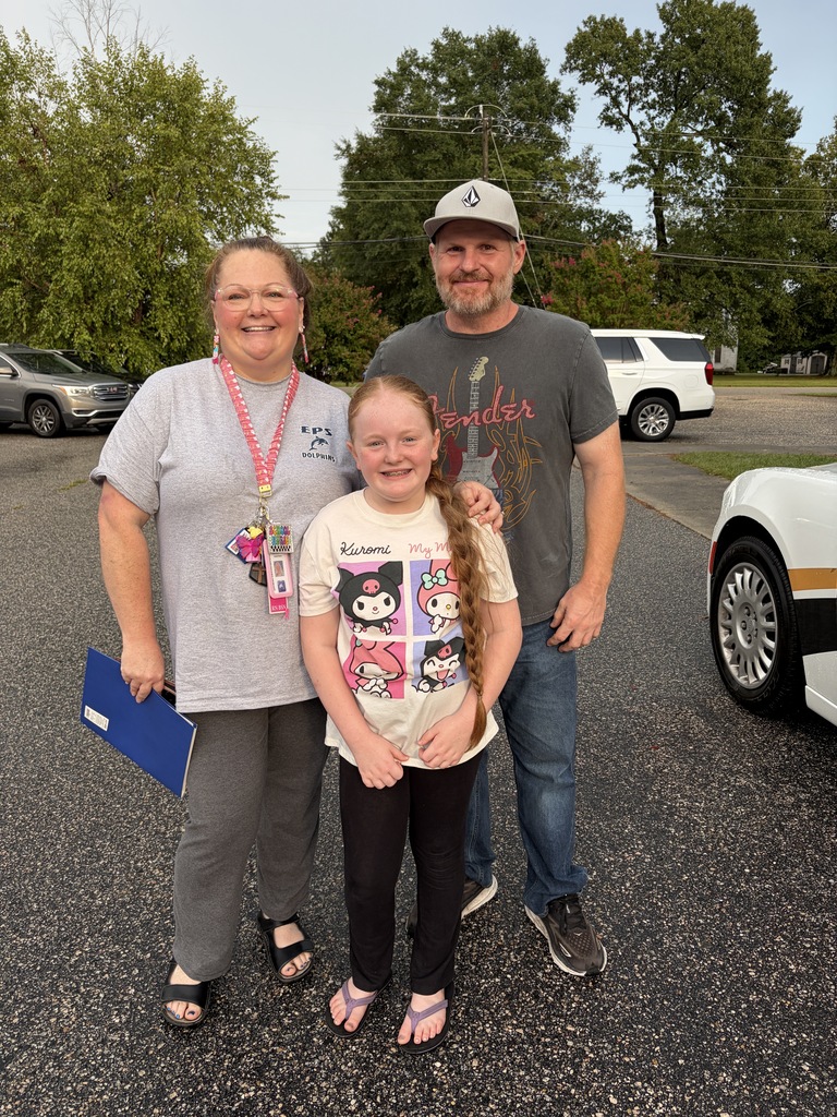 A family smiling in the parking lot outside of a school.