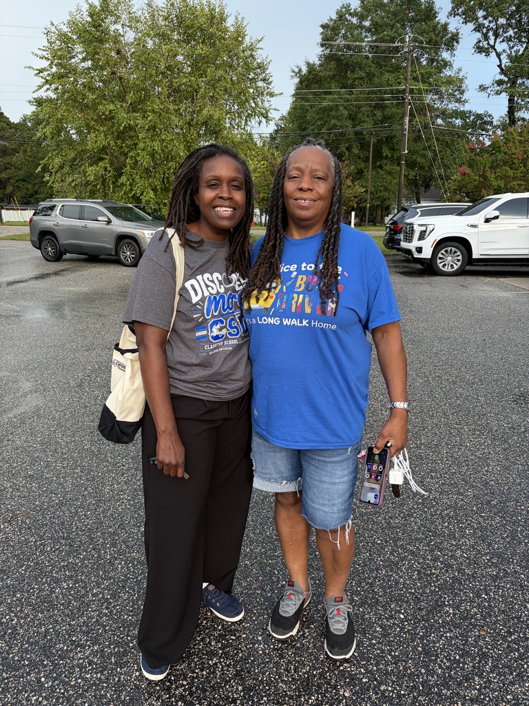 Two  school bus drivers stand outside smiling. 