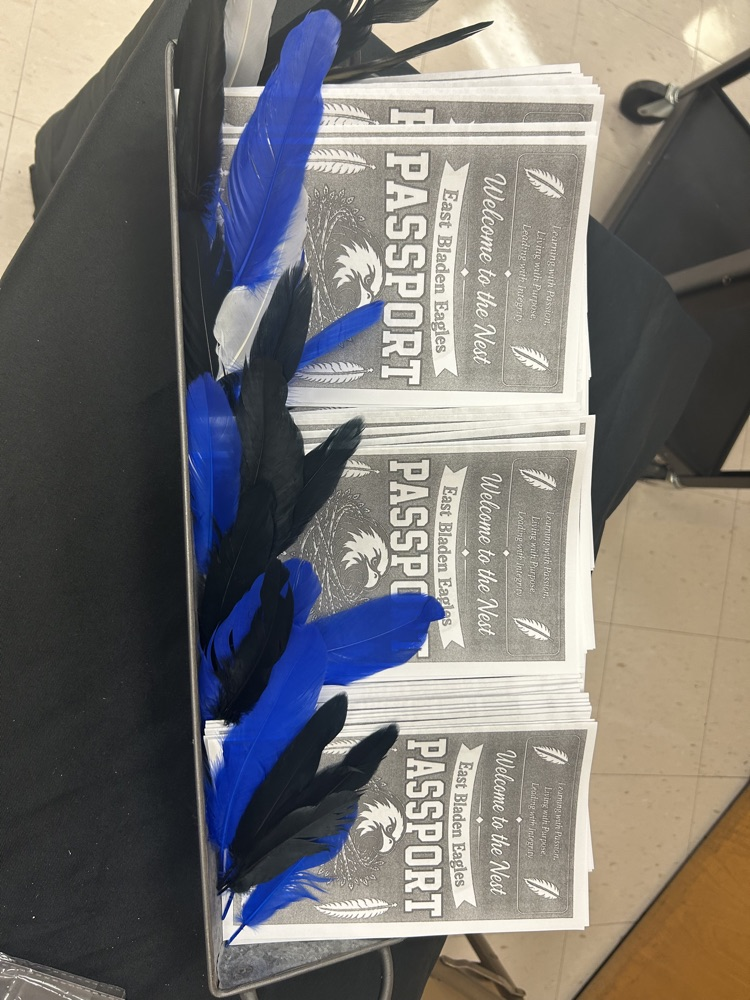 Metal basket on table with black tablecloth with East Bladen, high school, passports inside and blue and black feathers