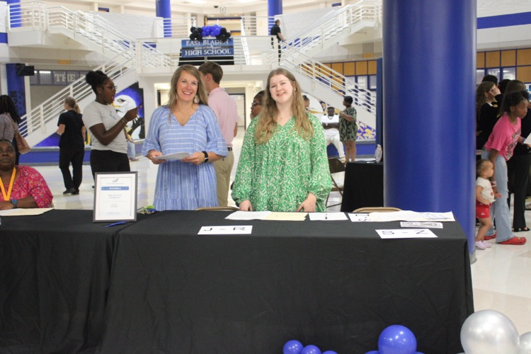 teacher and blue and white dress teacher and green and white dress standing behind a table with a black tablecloth, welcoming guest as they arrived to open house