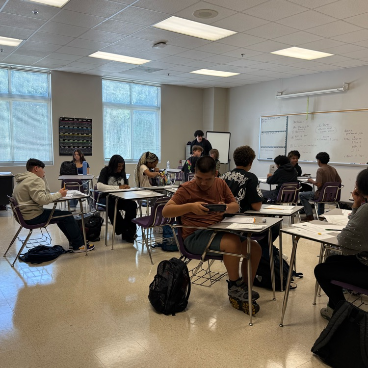 a class of students sitting in groups worjubg on an assignment 