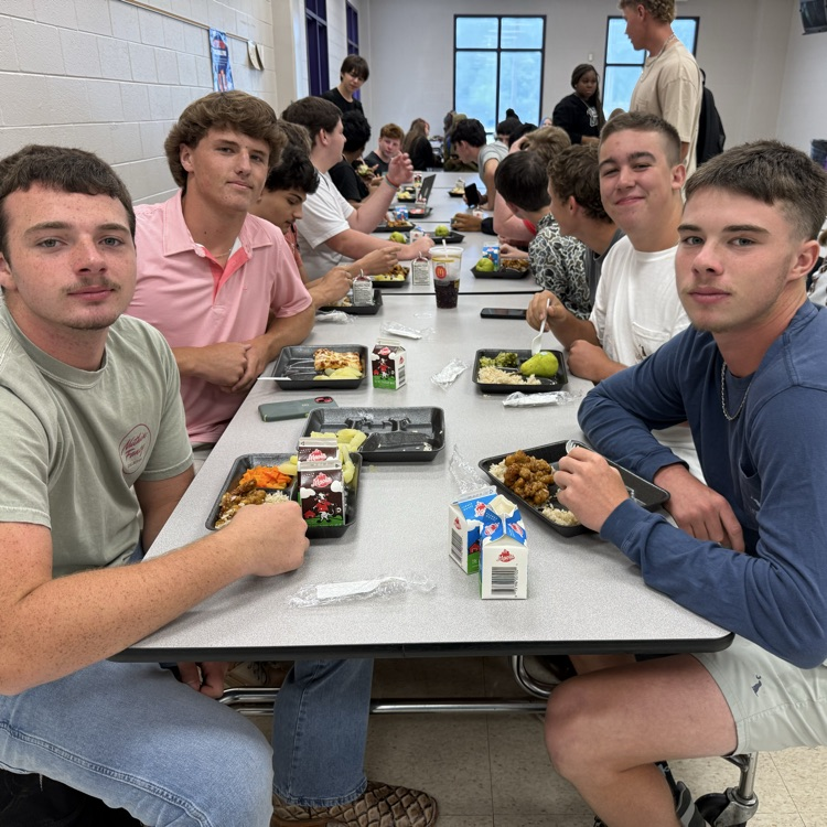 4 males pose at a cafeteria table while eating lunch 