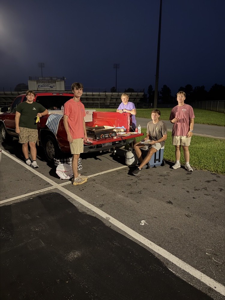 A group of teenagers staying around the bed of a truck as they cook breakfast and fellowship together