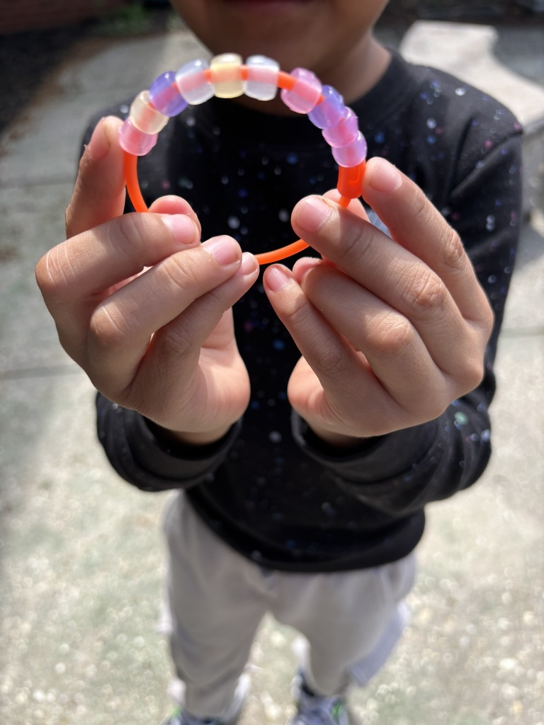 Student proudly holds up a colorful magic bead bracelet.
