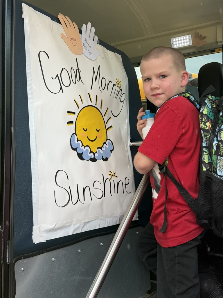 Student boards a school bus beside a cheerful “Good Morning Sunshine” sign with positive messages.